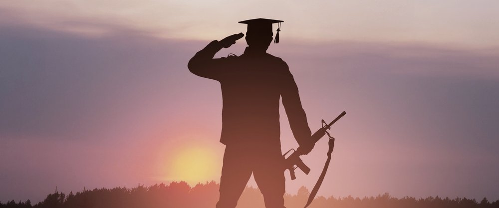 A soldier in a graduation cap saluting at sunset